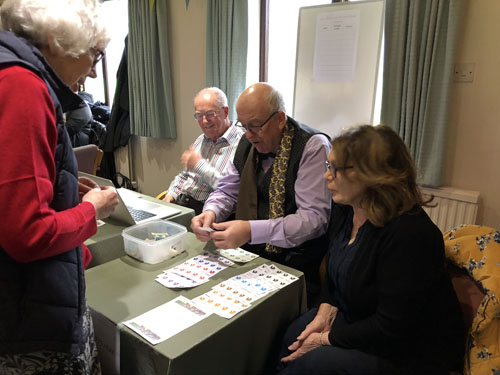 Alan selling betting tickets to Barbara  watched by Thora and Geoff