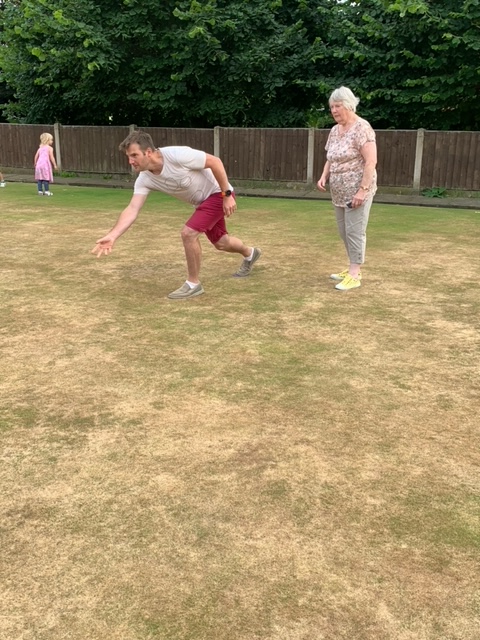 Man having a go at bowls, watched by Club Member