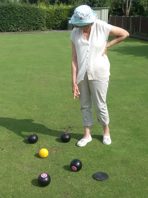 Sheila standing on the green pointing down at four woods and a jack.