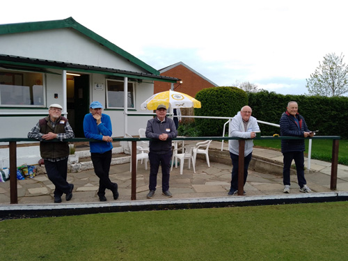 Five male bowlers standing in a line leaning on the railings outside the Tarvin clubhouse