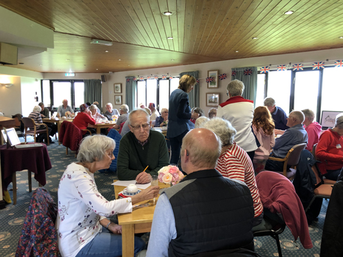 The Clubhouse full of people at tables, working on the Royal Quiz.