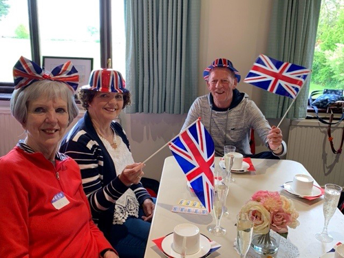 Margaret, Jackie and Roy. Margaret is wearing a Union Jack bow in her hair. Jackie and Roy are wearing Union Jack bowlers and waving flags.