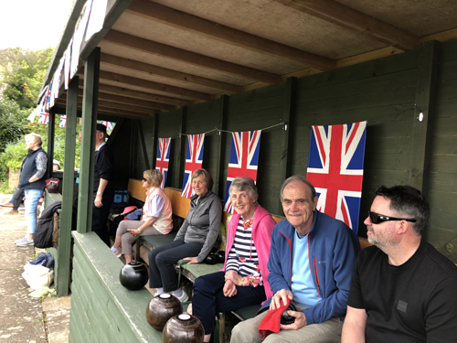 Len, Brenda, Sue, Chris, Rod & Mark in the hut watching games. Four large Union Jacks are hanging on the back wall.