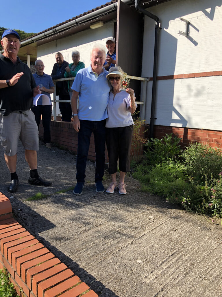 Brian and Brenda pose with the trophy on the ramp down to the field. Bob standing next to them and other Club members behind them.