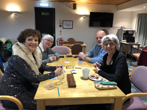 Jackie, Karen, Richard and Sheila at the Cards table, in the middle of a Cribbage game, smiling at the camera