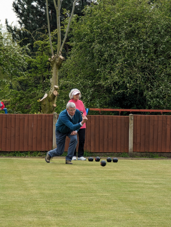 One male bowler delivering a wood. One female bowler standing behind him watching