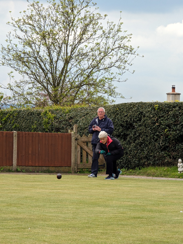 One female bowler delivering a wood. One male bowler standing behind her watching