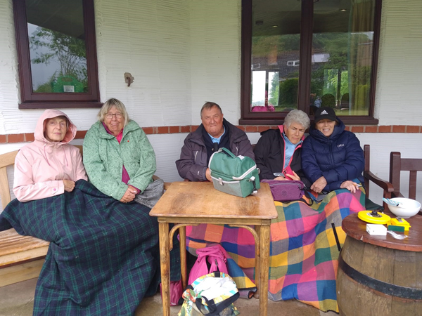 Four ladies and one man all bundled up in coats and blankets under the eaves of the Clubhouse