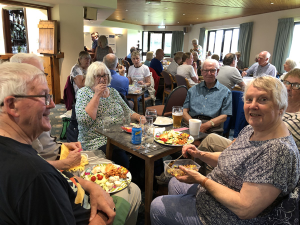 Members sitting at a table with picnic food on plates.