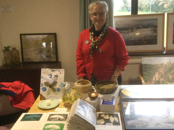 Anne standing behind a table with artwork, sculpture, turned bowls.