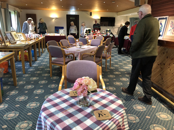 Getting ready for the afternoon. Tables set out iin the middle of the room with cloths, flowers, coasters. Around the outside tables with artwork, wood turning, knitting etc. Artists getting ready.