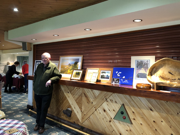 Barry standing by artwork displayed on the bar.