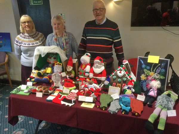 Maggie, Pat and Chris by the table of knitted Christmas items and shawls.