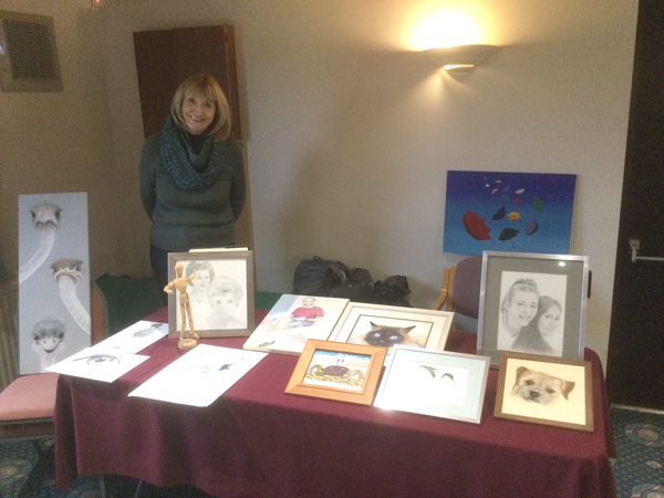 Laura standing behind a table filled with her paintings and drawings.