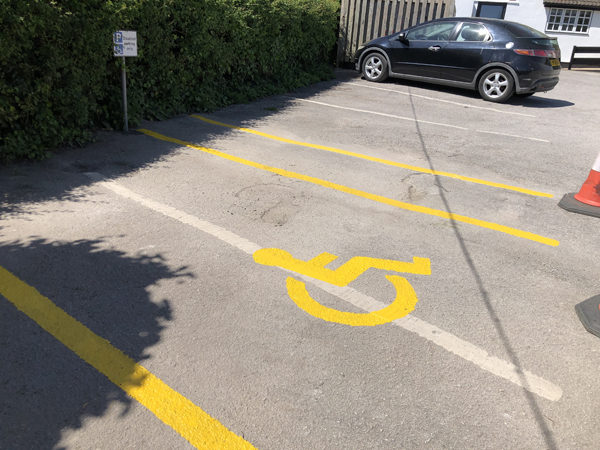 A disabled parking bay - yellow wheelchair icon between two yellow lines. A third yellow line to the top right - the space for unloading, not yet with diagonal lines