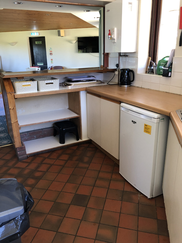 Picture of the entrance to the Clubhouse kitchen with tidy top shelf and empty shelves beneath