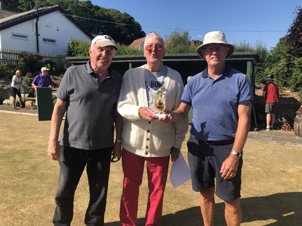 Three men standing on the green posing with the trophy