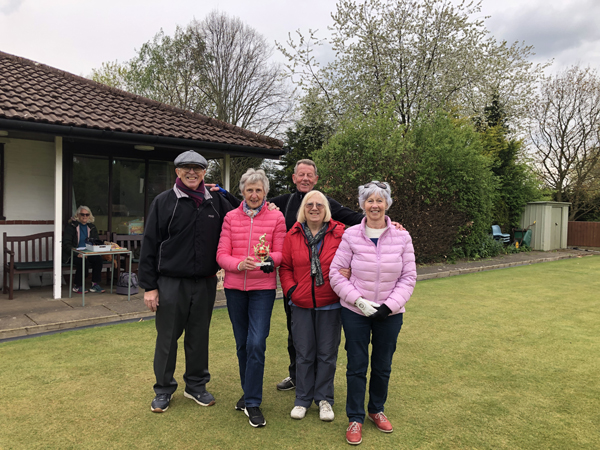 Three women and two men standing on the green, posing with the trophy