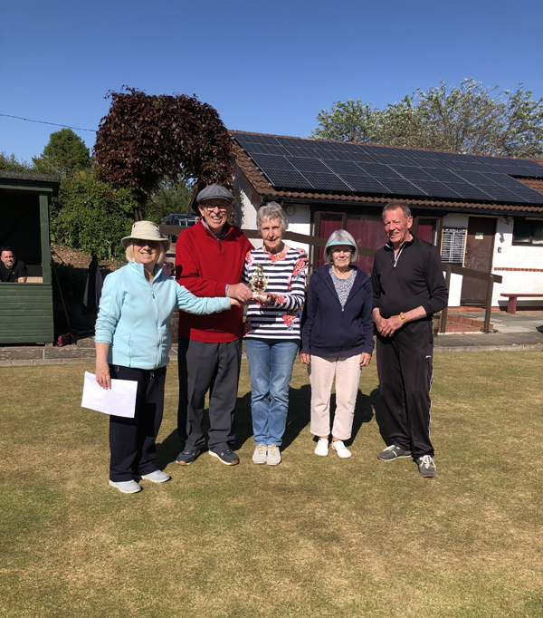 Three women and two men on the green, posing with the trophy