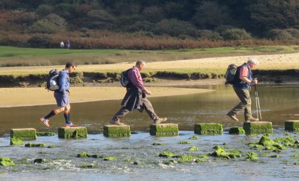 Three walkers crossing a river using stepping stones.
